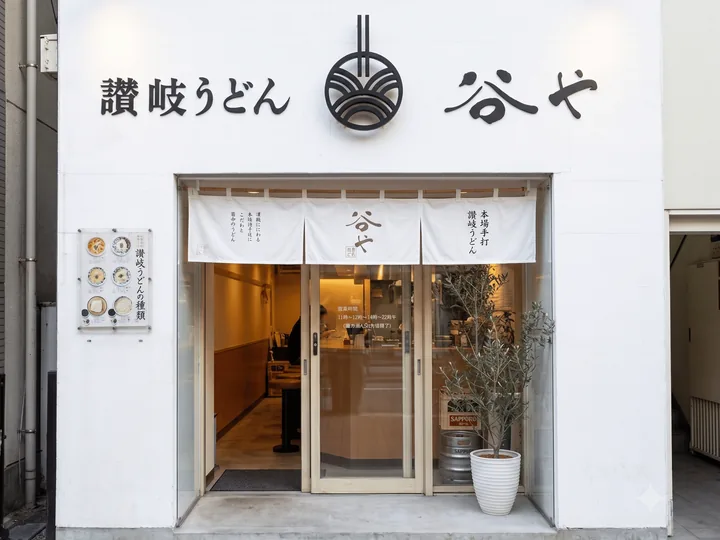 本店「讃岐うどん 谷や」（日本橋人形町）の外観。白い壁に波紋の紋章と暖簾