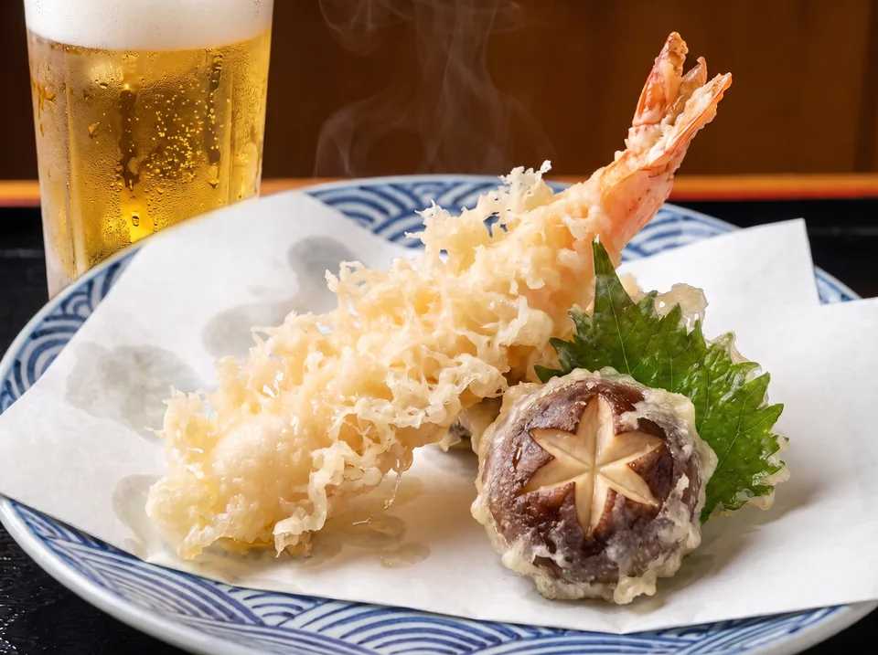 花咲く薄衣の大海老天と飾り切りの椎茸天、よく冷えたビール。青海波紋様の器に白い敷紙、湯気が立ちのぼる